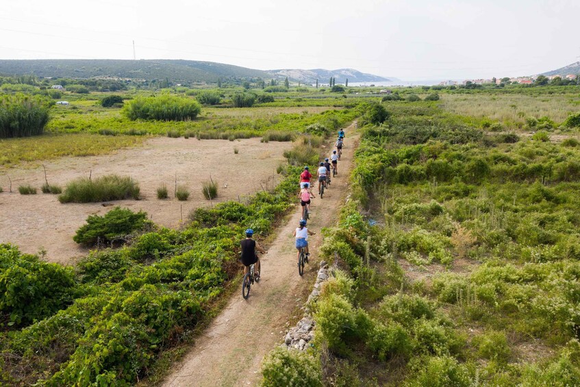 A group of cyclists on a dirt path through a grassy landscape with hills in the distance. 4