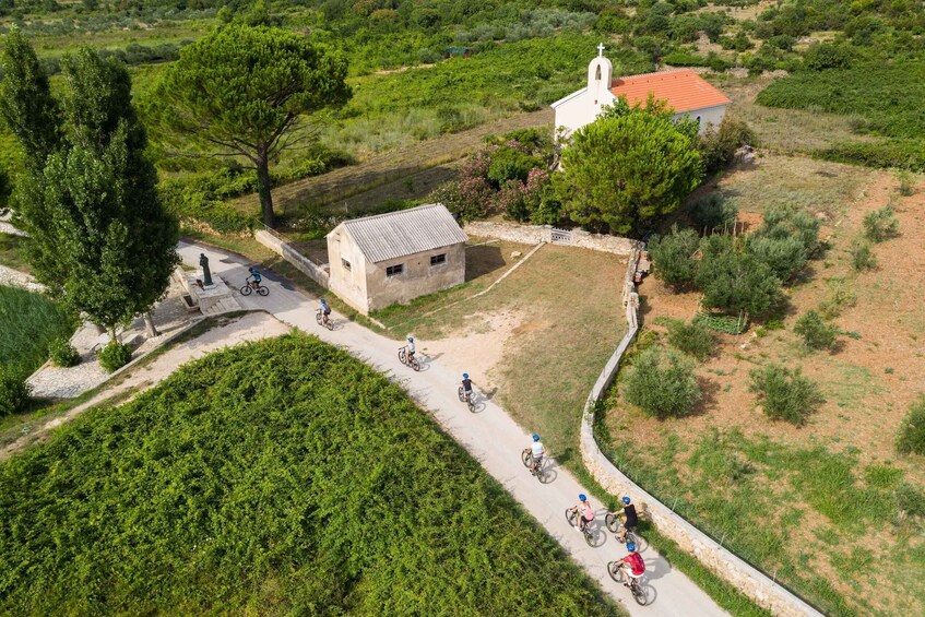 A rural landscape with a paved path, a white church, and cyclists. 1