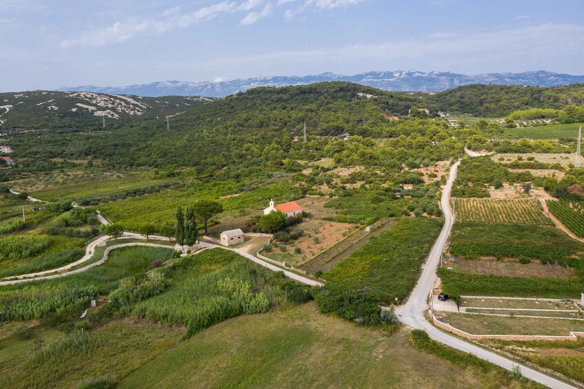 A rural landscape with winding roads, agricultural fields, a church, and distant mountains. 5