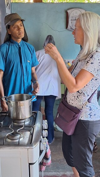 A woman in a patterned top and a man in a blue shirt standing by a stove with a pot. 3