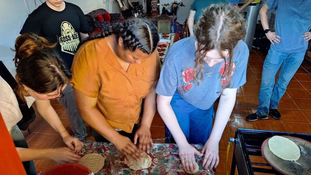 A group of people preparing food, with a focus on dough being rolled out on a table. 1