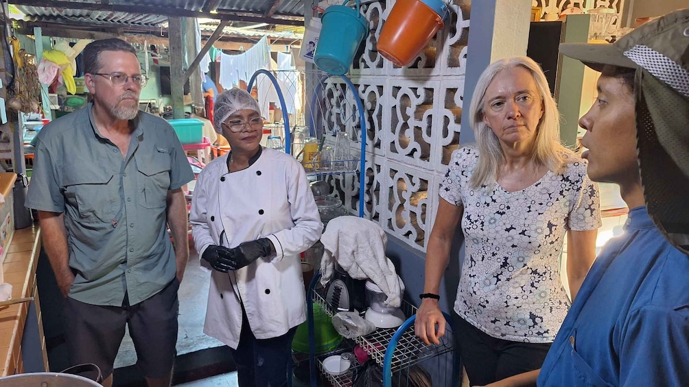 A group of people in a market setting with various items and a decorative wall in the background. 5
