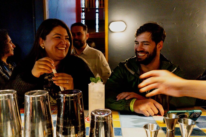 A group of people at a bar with drinks and a tall glass with a mint garnish. 1