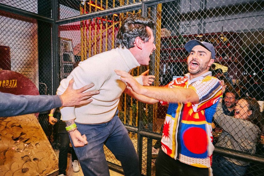 A person in a colorful shirt being held by another person in a cage-like structure. 3