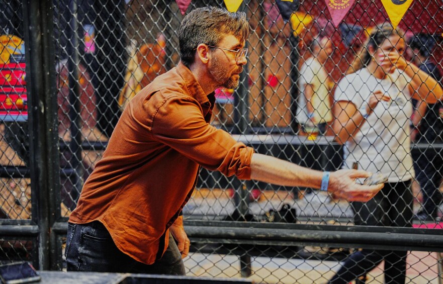 A man in an orange shirt playing a game behind a chain-link fence. 4