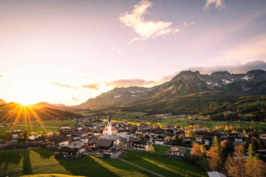 A mountainous landscape with a village, a church, and a sunset. 1