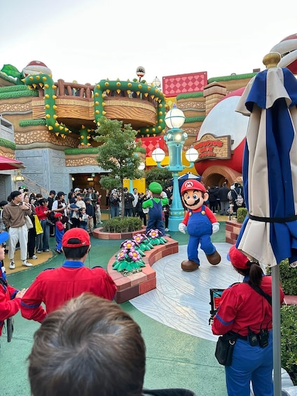 Un parco a tema con un personaggio di Mario, un edificio con un cartello che dice 'Nopios Cafe' e una folla di persone. 5