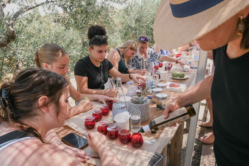 A group of people at an outdoor table with drinks, food, and a bottle being poured. 1