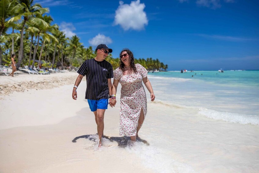 Two people walking on a sandy beach with palm trees and ocean in the background. 2