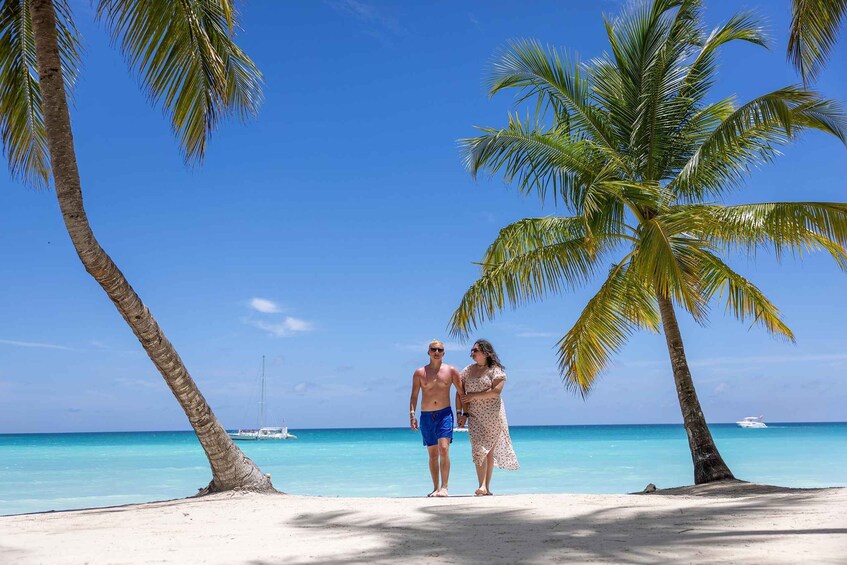 A couple walking on a beach with palm trees and a boat in the background. 4