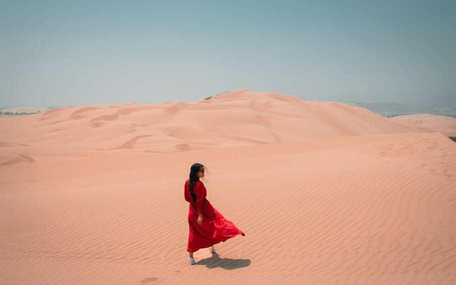 A person in a red dress walking on a sandy desert landscape. 1