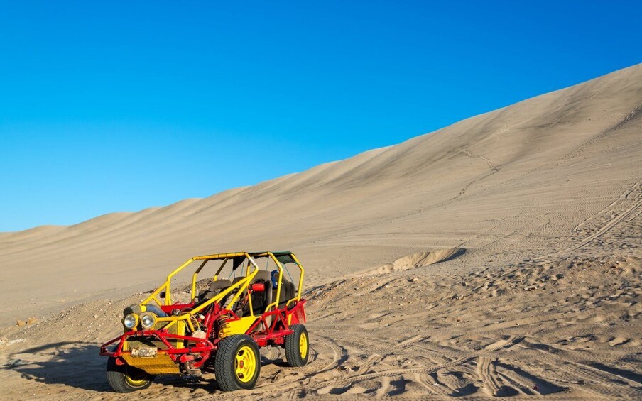 A yellow and red off-road vehicle in a desert with sand dunes. 5