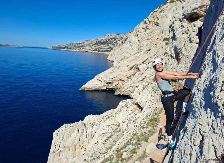 A person rock climbing on a coastal cliff with a clear blue sea in the background. 1
