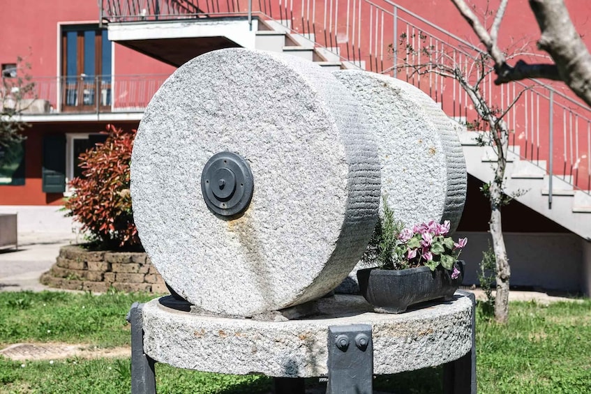 A large stone wheel with a black central hub, placed on a stone pedestal outdoors. 2