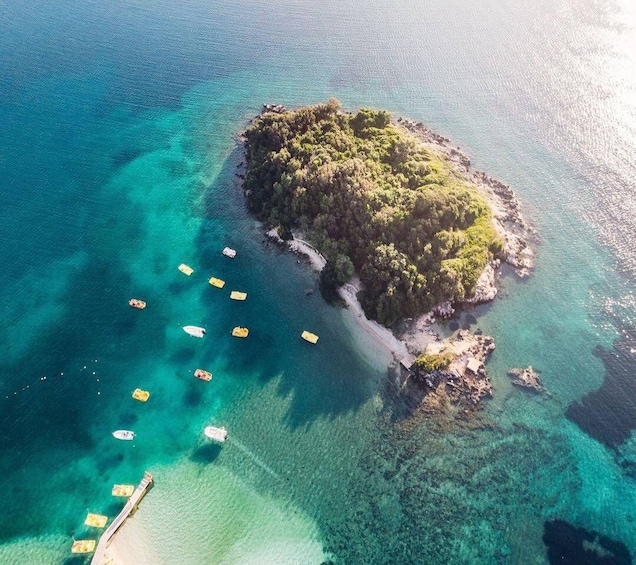 An island surrounded by clear turquoise waters with several small boats anchored near the shore. 4