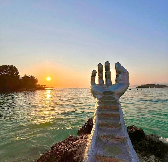 A hand sculpture by the water at sunset. 3