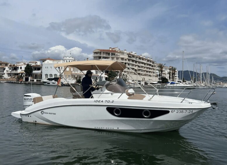 A white motorboat named 'IDEA 70.2' docked at a marina with buildings and boats in the background. 2