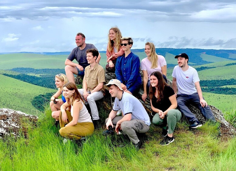 A group of people sitting on a grassy hill with a scenic view of rolling hills and a cloudy sky. 2