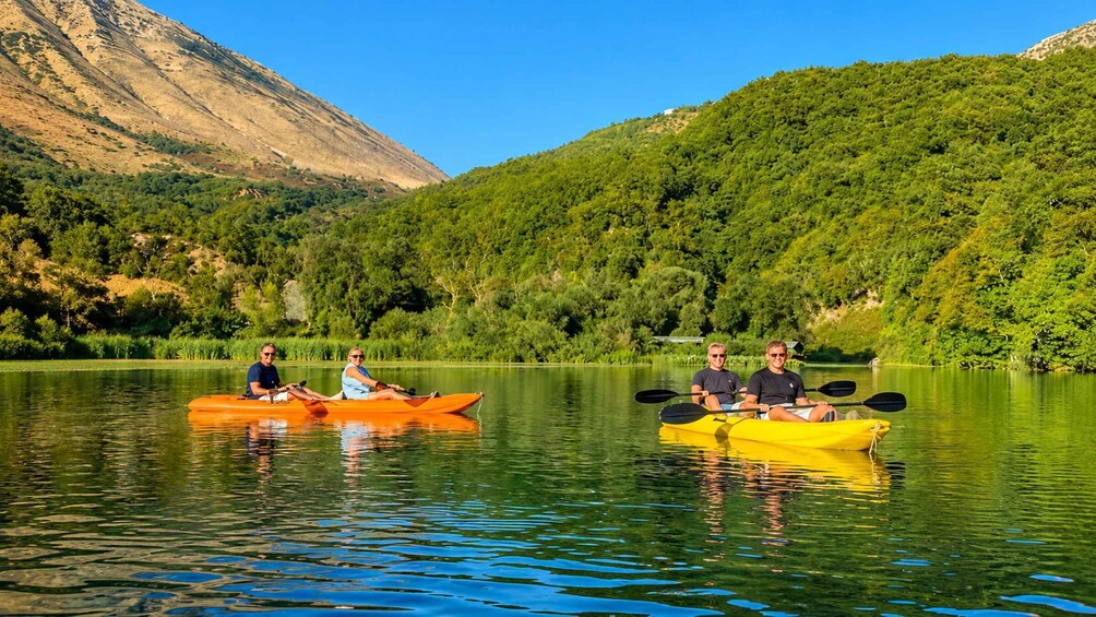 Three people kayaking on a calm lake surrounded by lush green hills. 1