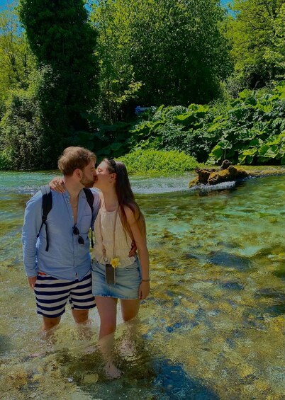 Two people standing in clear water with a forested riverbank in the background. 5