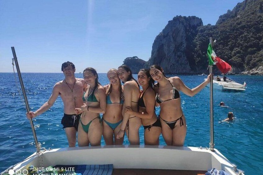 Un grupo de personas en un barco en un mar azul y transparente, con acantilados rocosos al fondo. 2