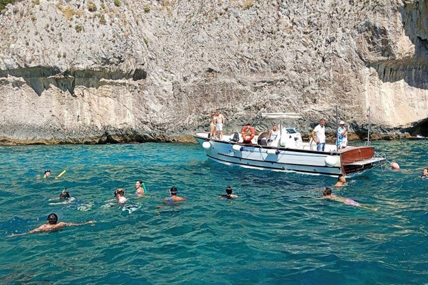 Un bote con gente a bordo y nadadores en el agua cerca de un acantilado rocoso. 1