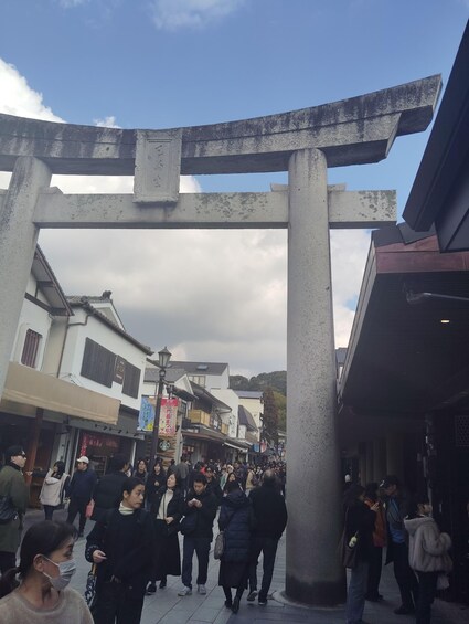 A bustling street with a large stone torii gate, shops, and pedestrians. 4