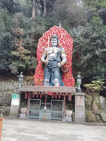 A statue with a red and gold backdrop, surrounded by stone lanterns and a stone wall. 2