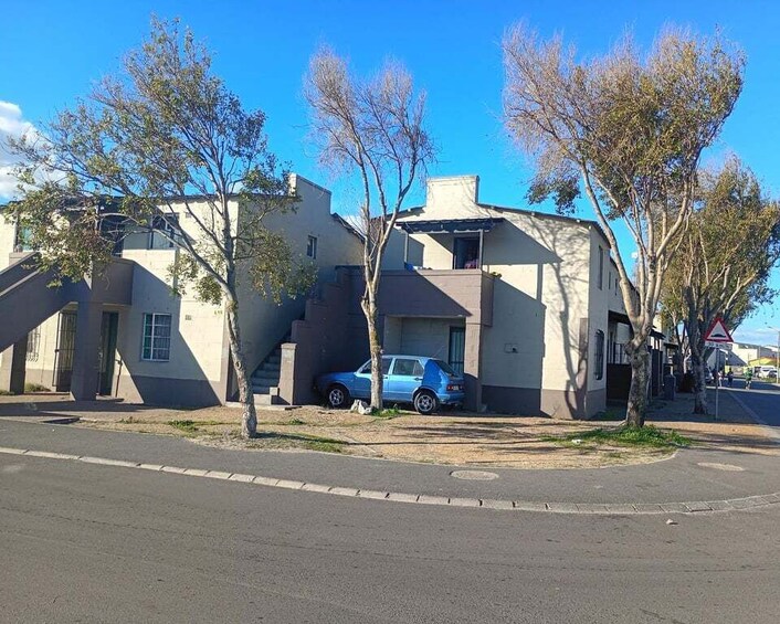 A residential area with a blue car parked in front of a house, surrounded by trees and a clear blue sky. 5
