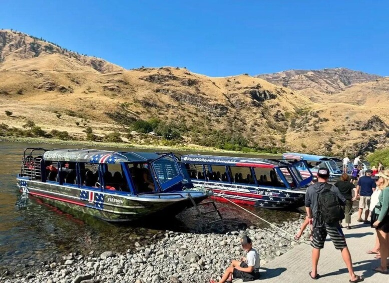 Two boats with American flag designs docked at a riverbank with people around. 3