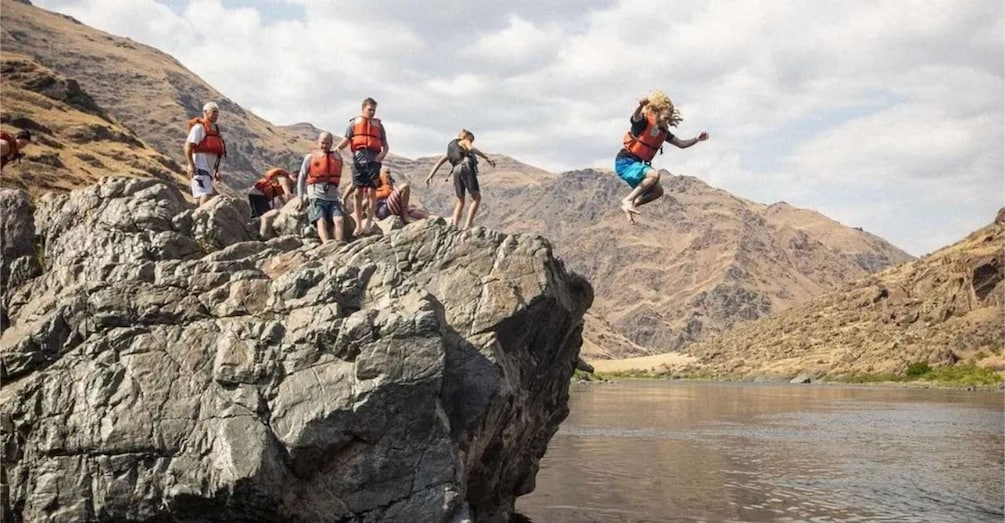 People jumping off a rocky cliff into a river. 5