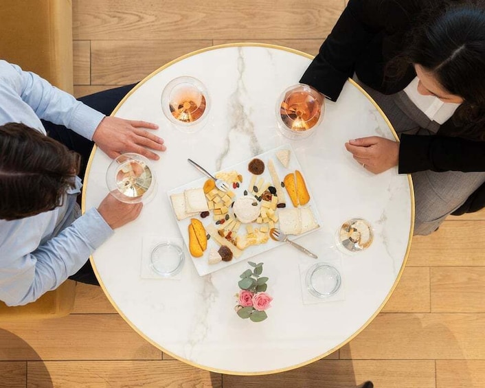 A group of people seated around a round table with a cheese board, glasses, and a small bouquet of flowers. 2