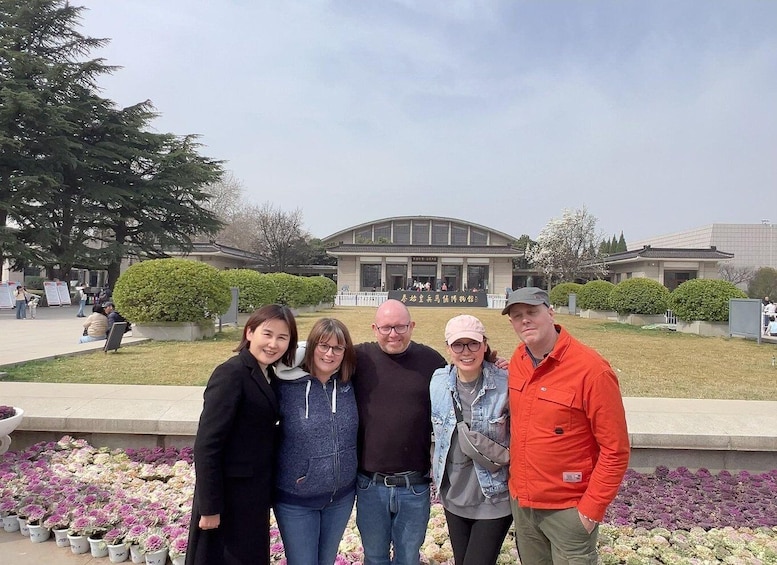 A group of people posing in front of a building with a large entrance and a lawn with flowers. 3