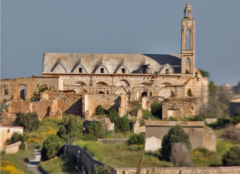 An ancient stone building with a bell tower, surrounded by overgrown vegetation. 2