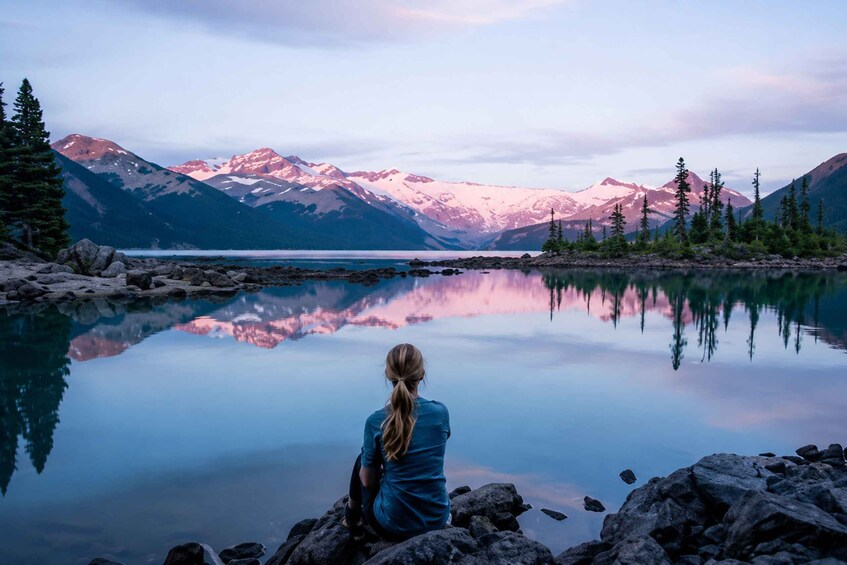 A person sitting on rocks by a calm lake with mountains in the background. 3