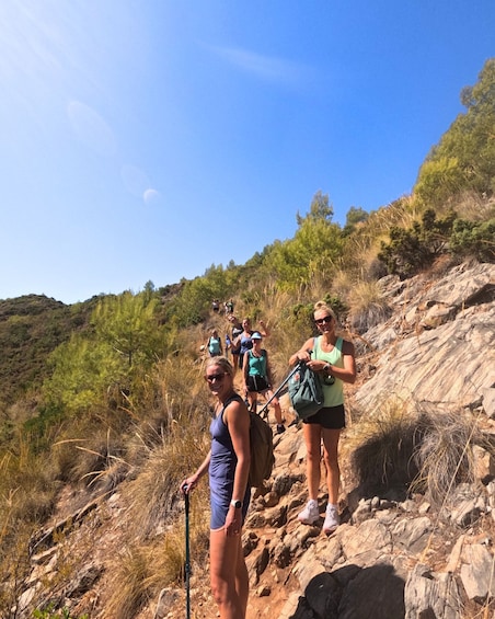 Hikers on a rocky trail with dry grass and trees in the background. 5