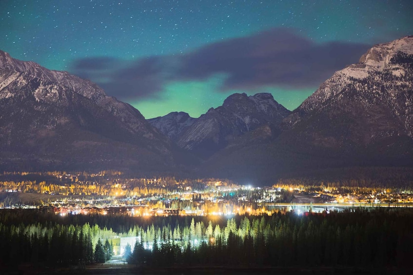 A night view of a town by a lake with mountains in the background and the aurora borealis. 1