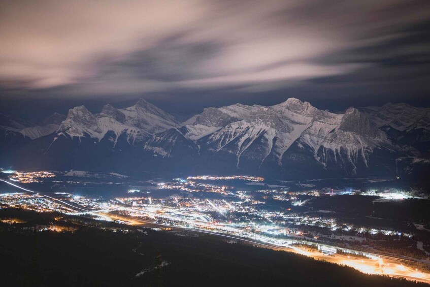 A snow-covered mountain range at night with a lit town below. 4