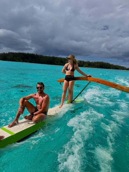 Two people on a wakeboard in turquoise water with a forested island in the background. 3