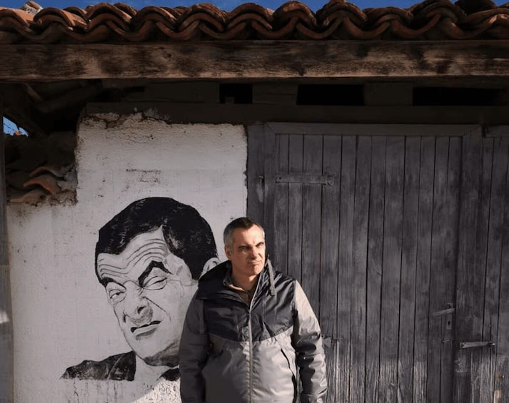 A man standing in front of a building with a mural and a wooden door. 3