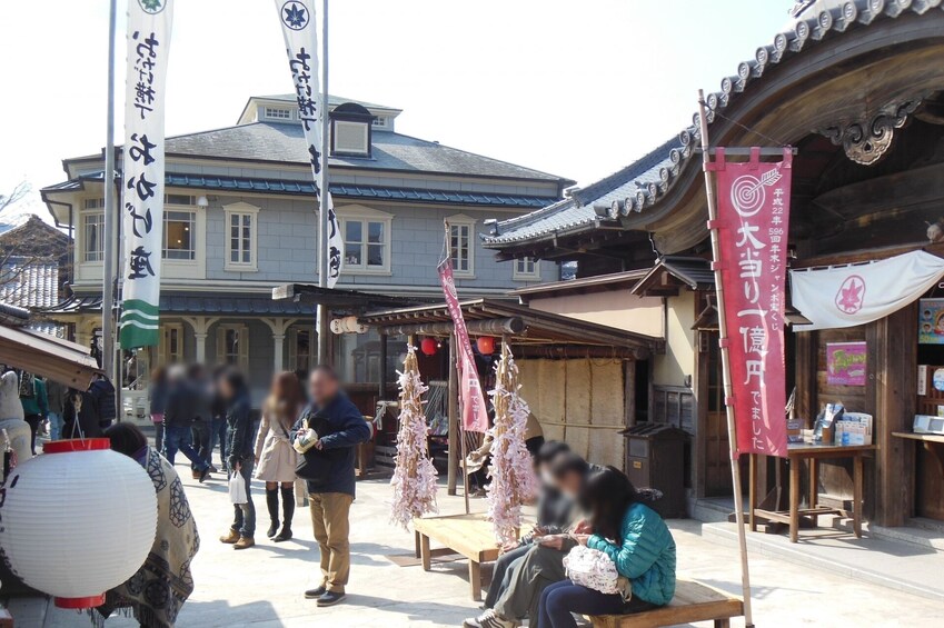A traditional Japanese street with people walking, a building with a tiled roof, and hanging decorations. 5