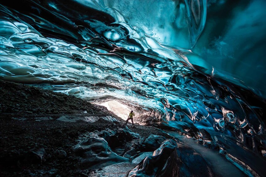 A person walking through a glacial cave with reflective ice surfaces. 1