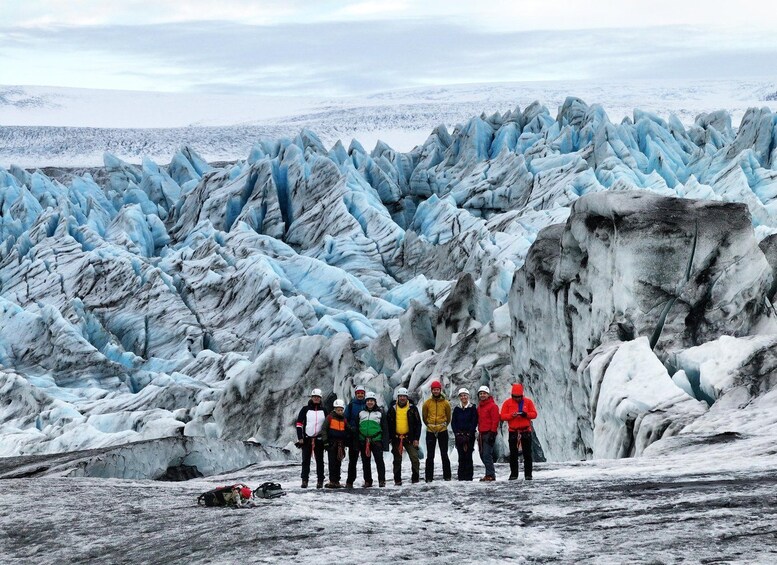 A group of people standing in front of a glacier with sharp, jagged ice formations. 3
