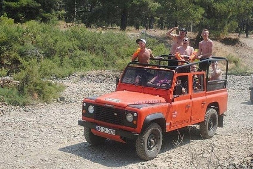 Un véhicule tout-terrain rouge, avec des personnes dessus, circule sur un chemin de gravier bordé de verdure. 3