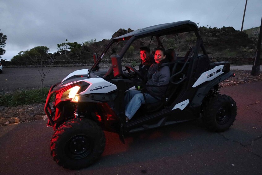 A Can-Am Maverick ATV parked on a paved area with a rocky hillside in the background. 1
