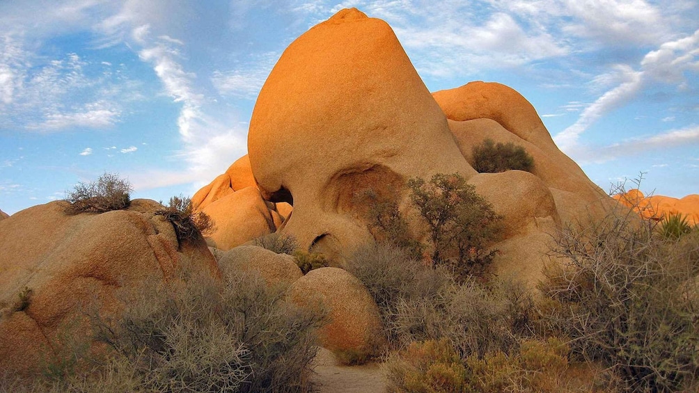 A large, conical rock formation with a cave entrance, surrounded by sparse desert vegetation. 3