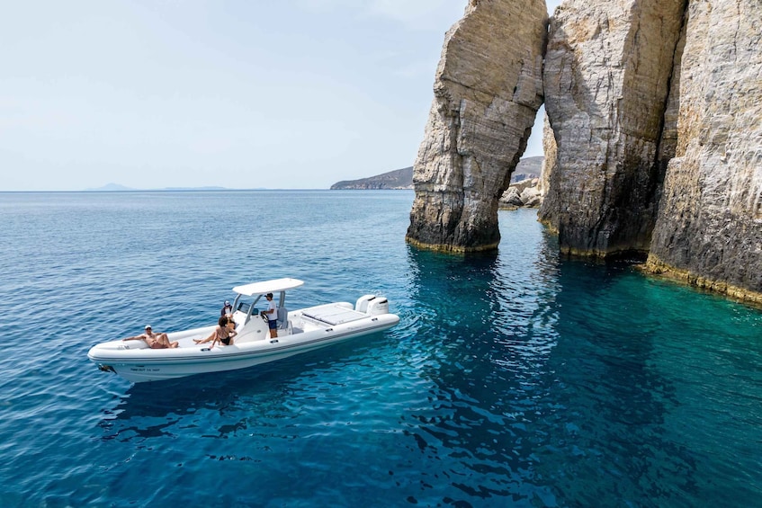A boat with people on a clear blue sea near rocky cliffs. 1
