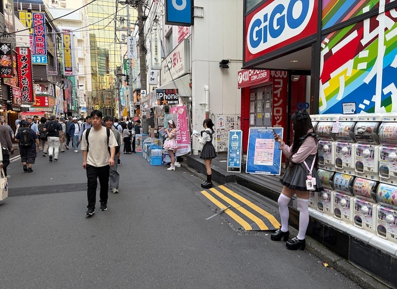 A busy urban street with pedestrians, a GIGO store, and vending machines. 5