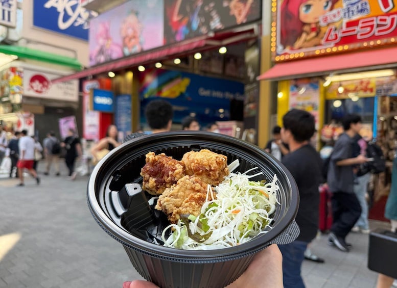 A hand holding a meal with fried chicken and coleslaw. 1