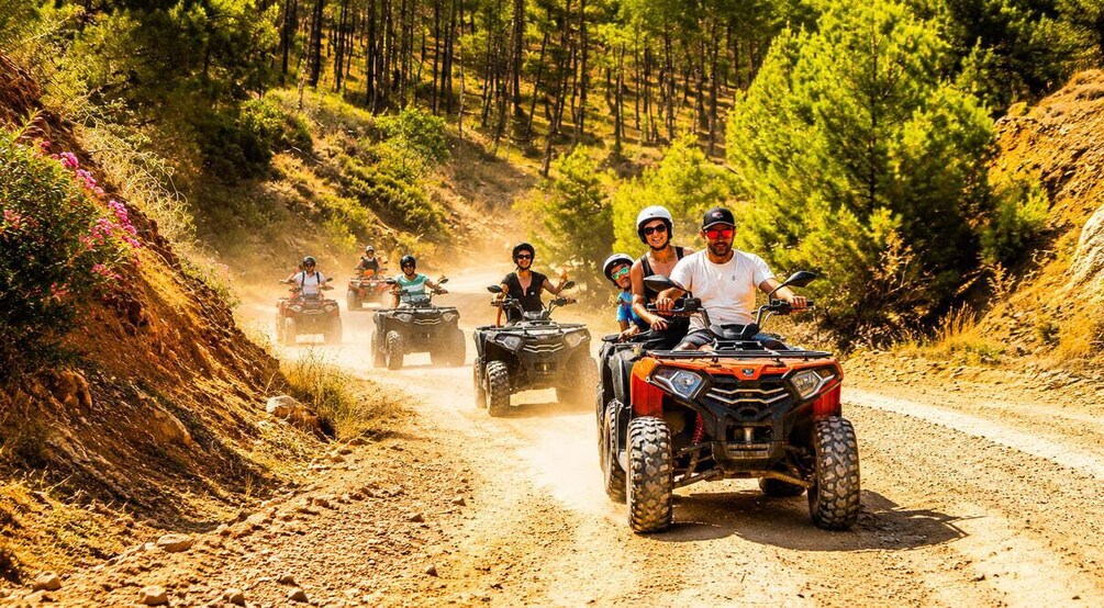 A group of people riding ATVs on a dirt road surrounded by trees. 3